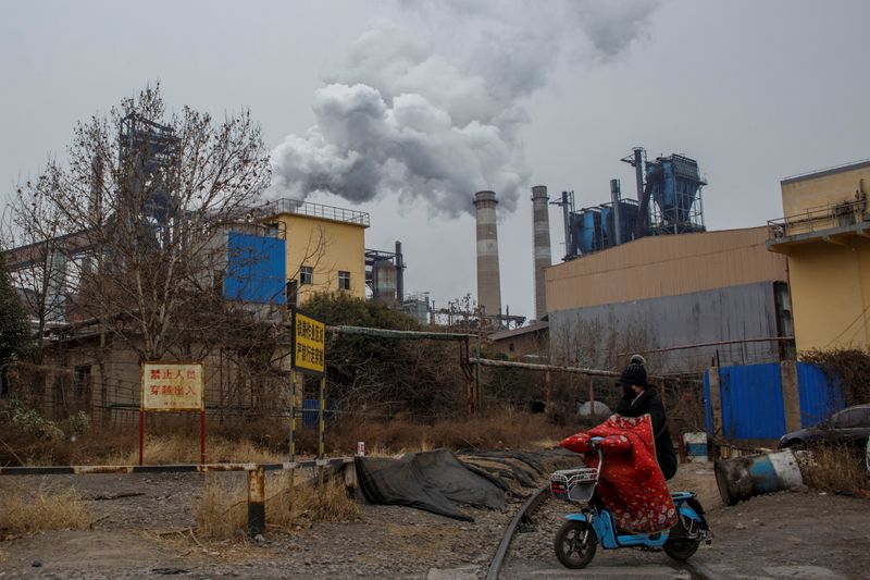 A woman rides a scooter past a steel plant in