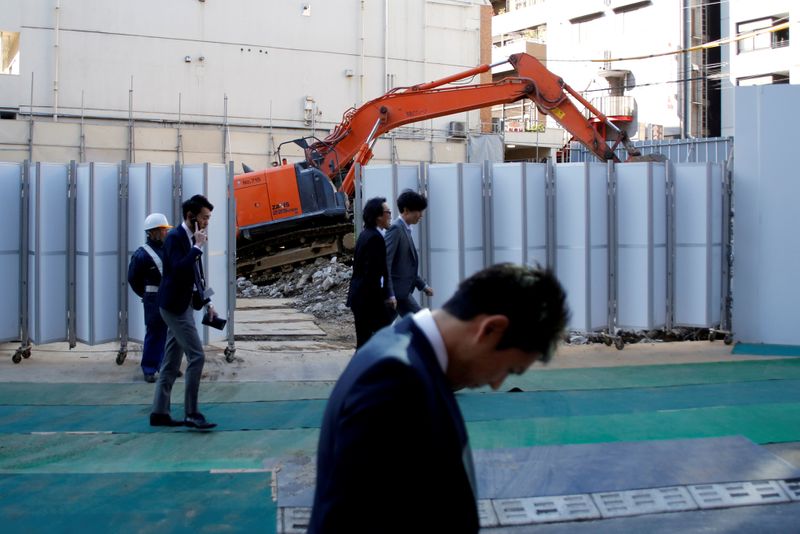 FILE PHOTO: Businessmen walk past heavy machinery at a construction