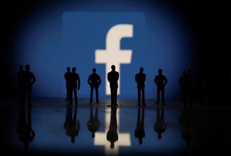 Small toy figures are seen in front of displayed Facebook