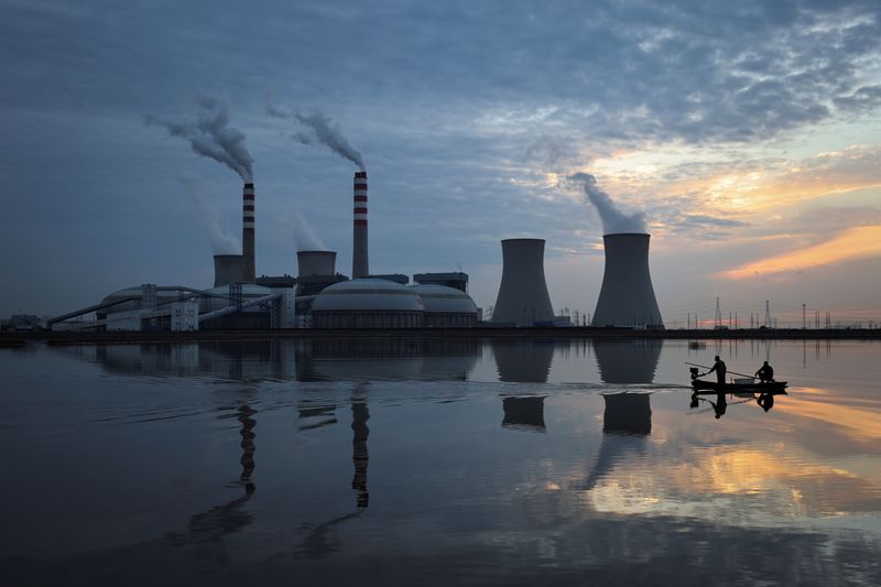 Fishermen sail a boat past a power plant of the