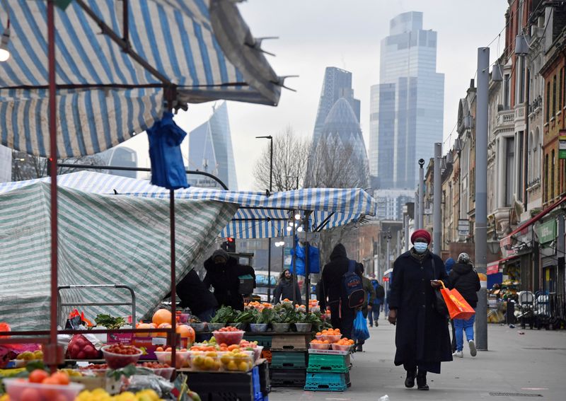 People shop at market stalls, with skyscrapers of the CIty