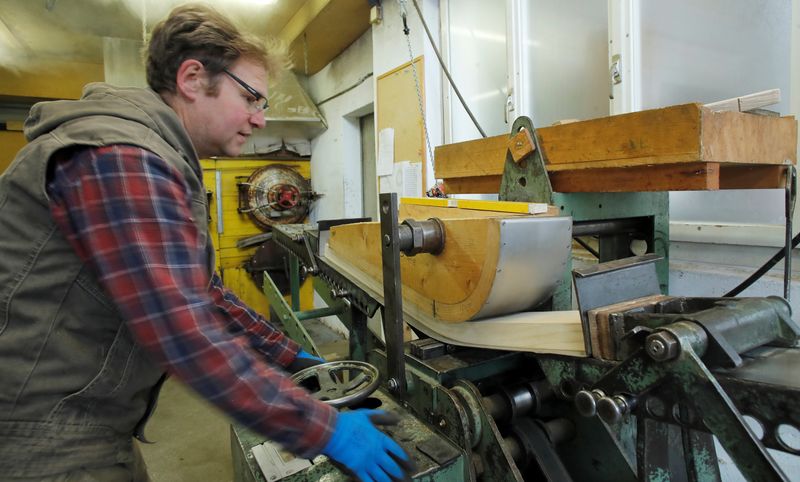 A worker uses a machine to shape heated wood to