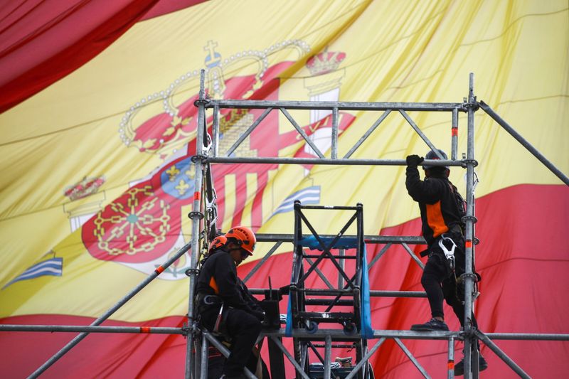 Workers set up a scaffold as a Spanish flag flutters