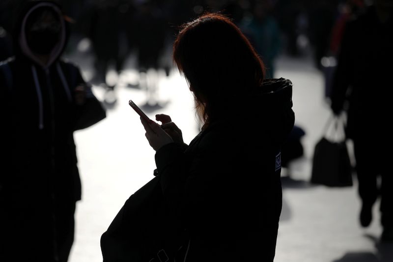 FILE PHOTO: A woman checks her phone as passengers arrive