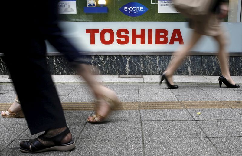 Pedestrians walk past a logo of Toshiba Corp outside an
