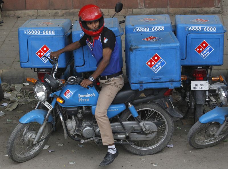 An employee rides a motorcycle to deliver Domino’s Pizza to