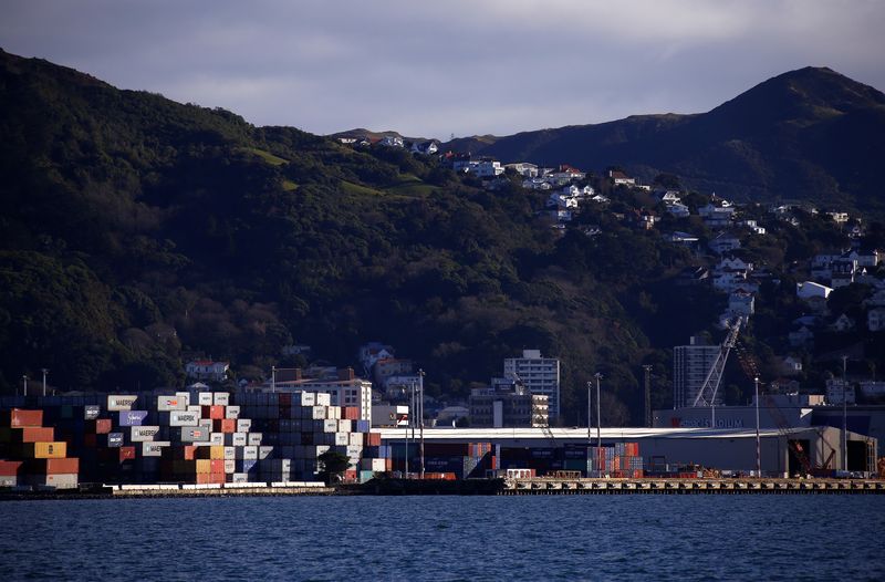 Containers sit stacked at a port terminal with residential houses