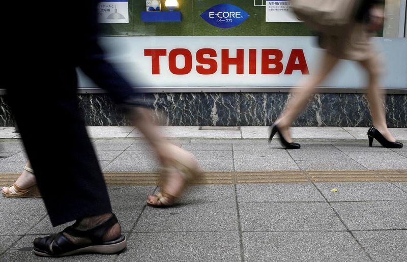 FILE PHOTO: Pedestrians walk past a Toshiba logo outside an