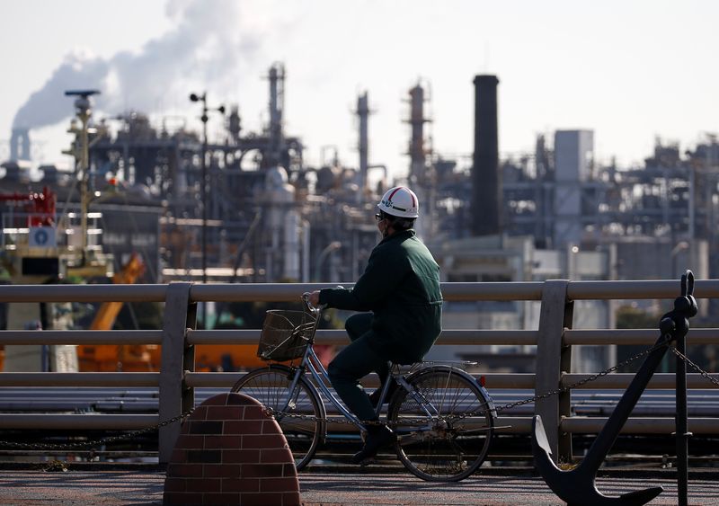 A worker cycles near a factory at the Keihin industrial