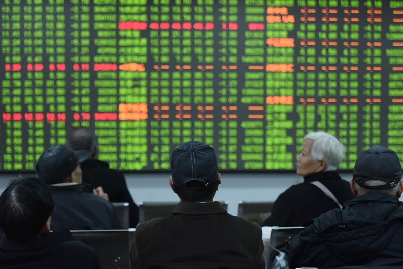 Investors sit in front of a board showing stock information
