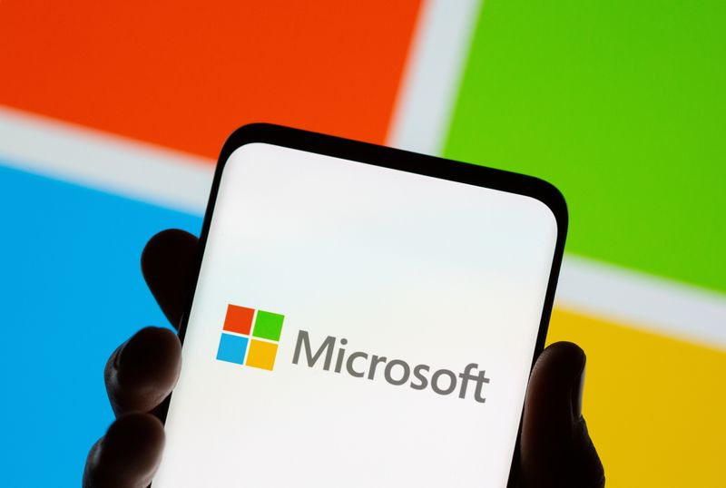 Smartphone is seen in front of Microsoft logo displayed in