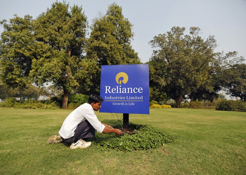 A gardener works next to a board of Reliance Industries