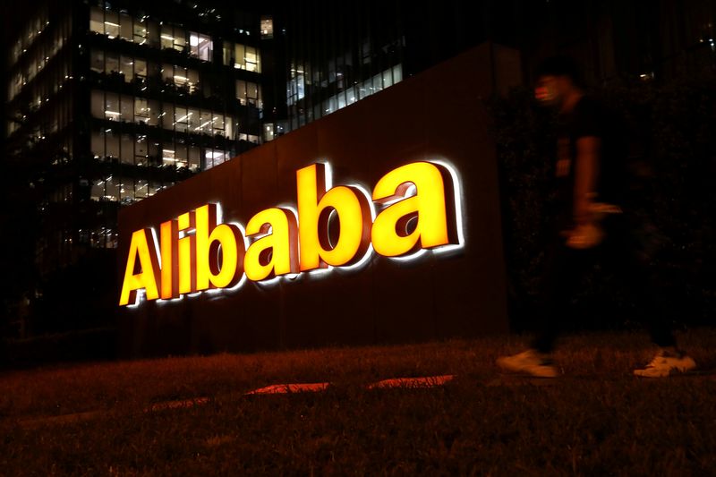 FILE PHOTO: Man walks past a logo of Alibaba Group