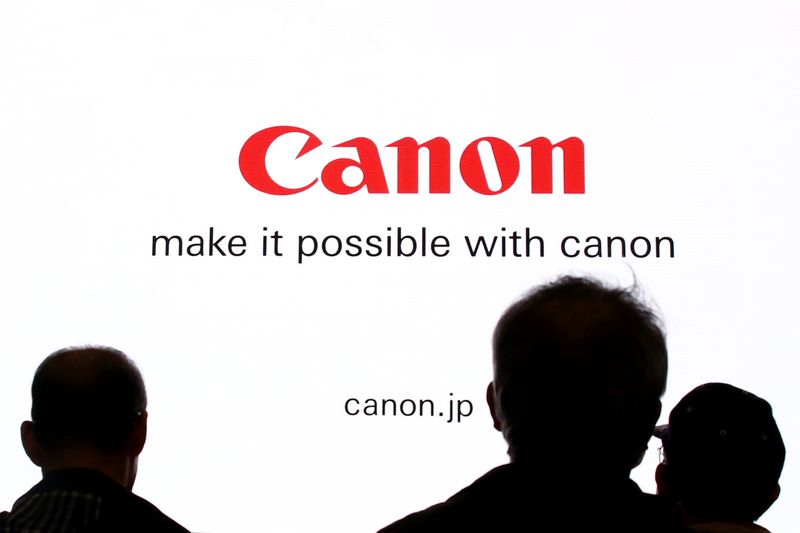 People are silhouetted against a display of the Canon brand