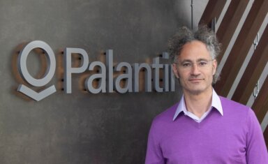 Karp, CEO of Palantir Technologies poses beside the company’s logo