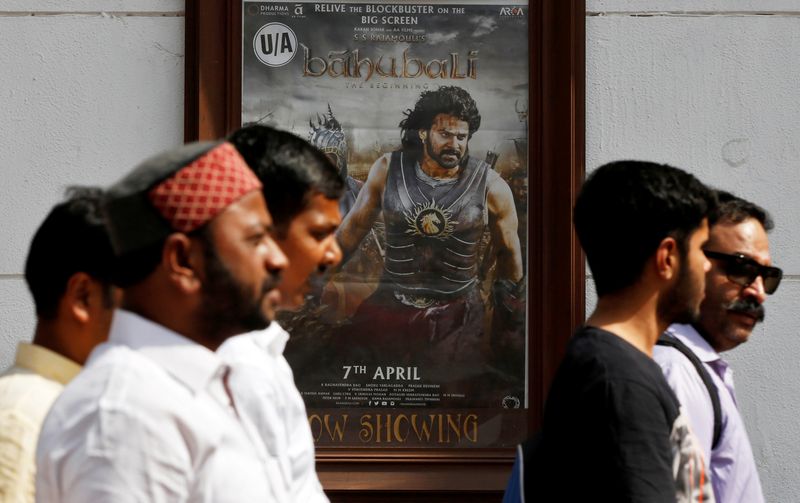 People walk past a poster of an Indian movie “Baahubali: