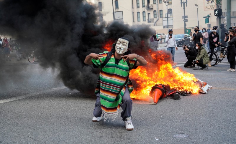 A masked protester stands in front of a fire during