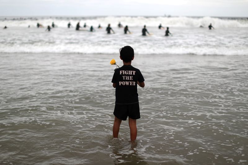 A boy holds a rose as he watches surfers at