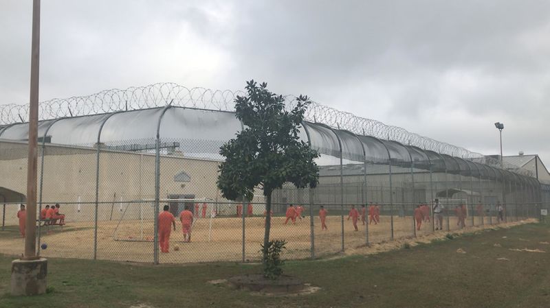 Detained immigrants play soccer behind a barbed wire fence at