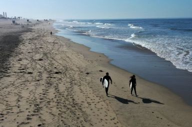 FILE PHOTO: Surfers walk into the Pacific Ocean at sunrise