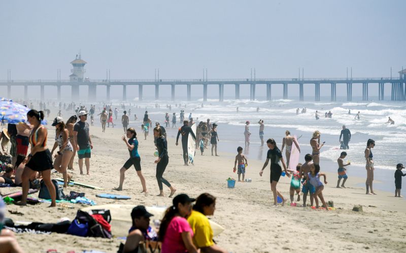 People walk up and down Huntington City Beach during the
