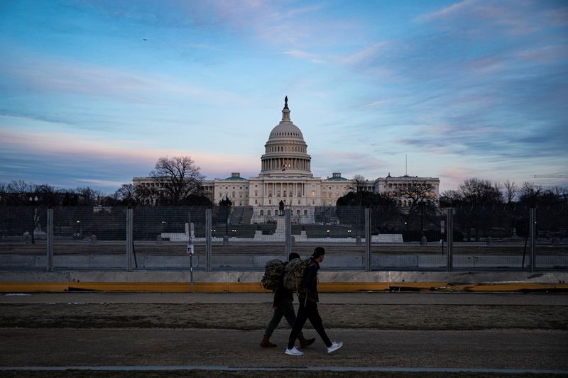 People walk past protective fencing surrounding the U.S. Capitol, as