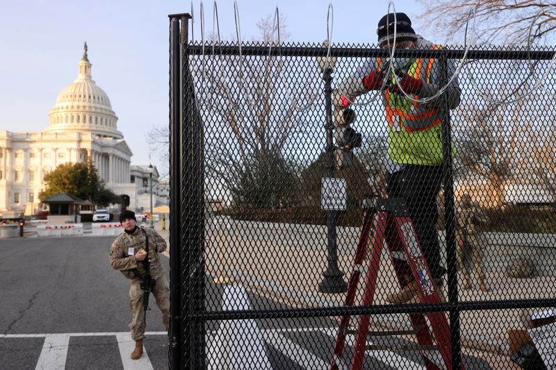 FILE PHOTO: Workers install razor wire atop the unscalable fence