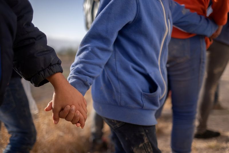 Asylum seeking unaccompanied minors hold hands amid adult migrants from