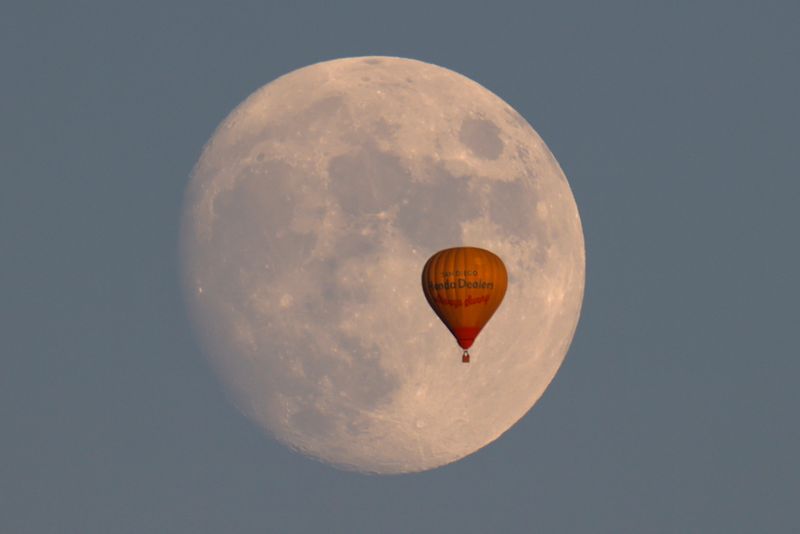 Hot air balloon floats past a rising moon in California