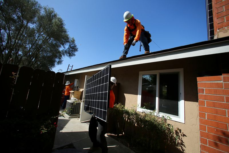 FILE PHOTO: Workers lift a solar panel onto a roof