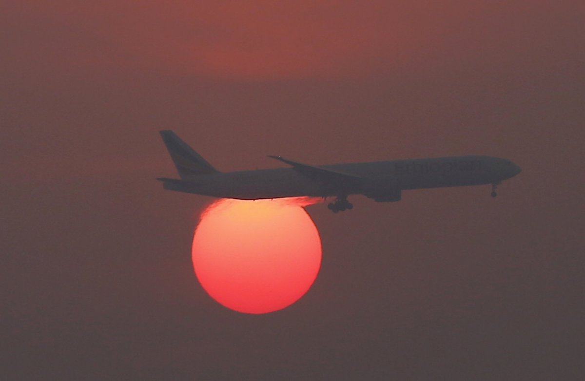 A plane flies over the setting sun in the sky