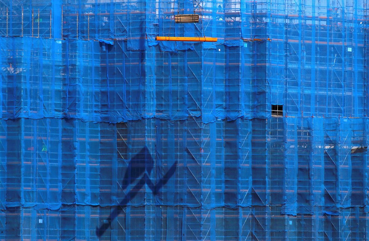 A crane lifts building materials in front of scaffolding at