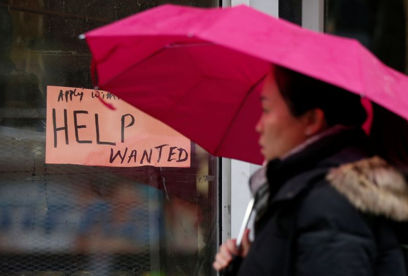 A woman walks past a “Help wanted” sign at a