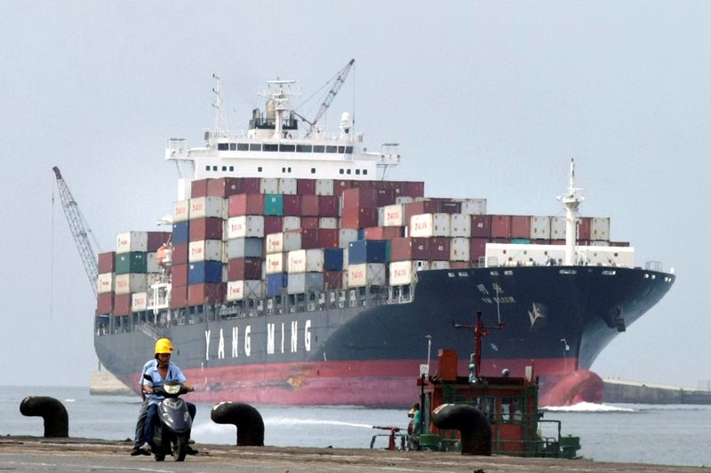 FILE PHOTO: People ride a motorcycle while a container ship