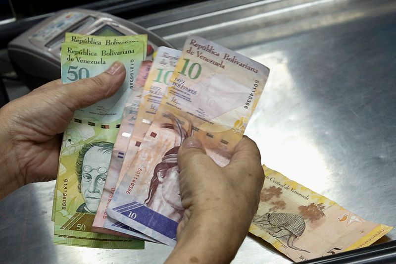 A cashier counts Venezuelan bolivar notes at a supermarket checkout