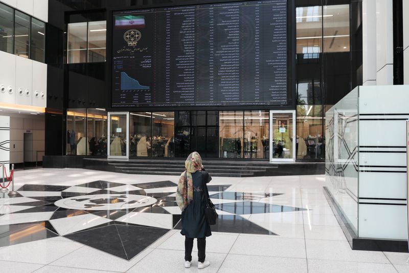 A woman looks at electronic board showing stock prices, following
