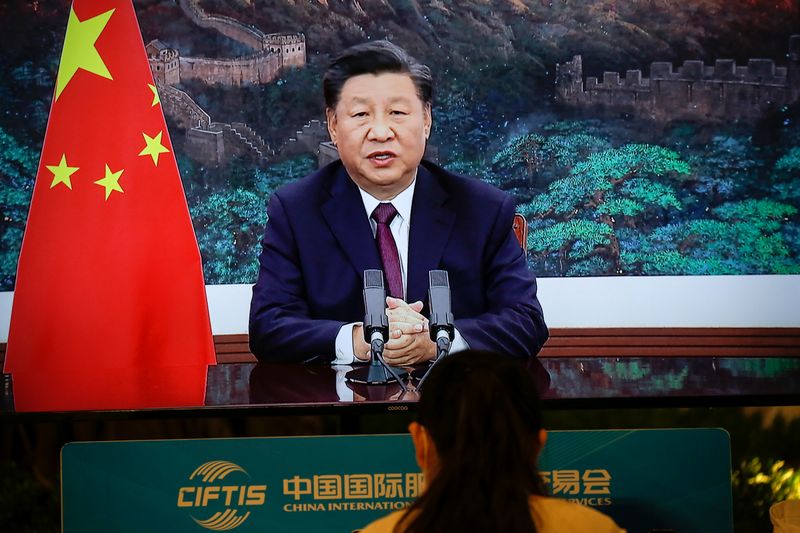 Journalist sits next to a screen showing Chinese President Xi