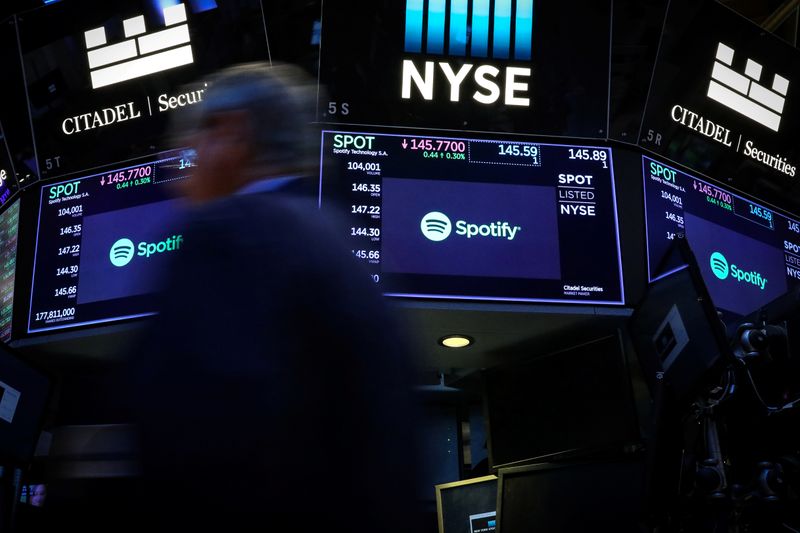 A trader passes by screens showing Spotify on the floor