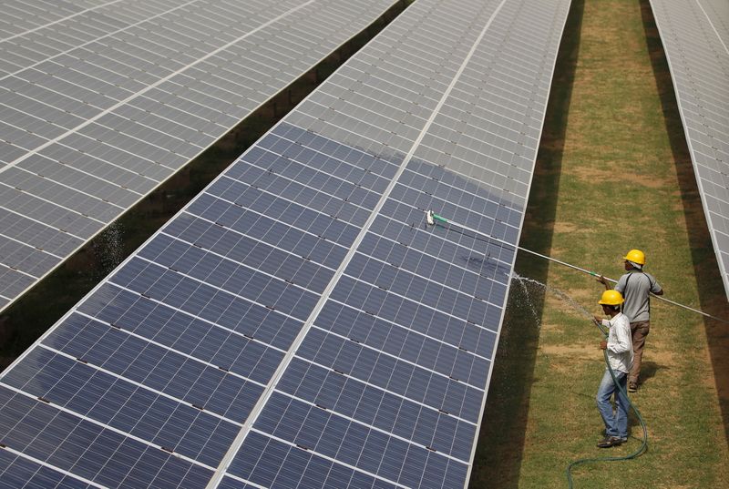 Workers clean photovoltaic panels inside a solar power plant in