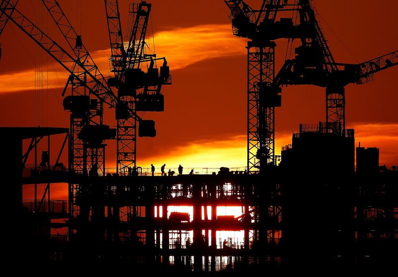 Workers are seen as the sun sets behind a construction