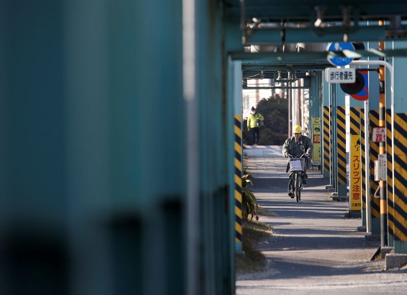 A worker cycles near a factory at the Keihin industrial