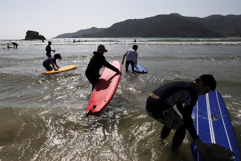 Surfers push their surfing boards as they head into the