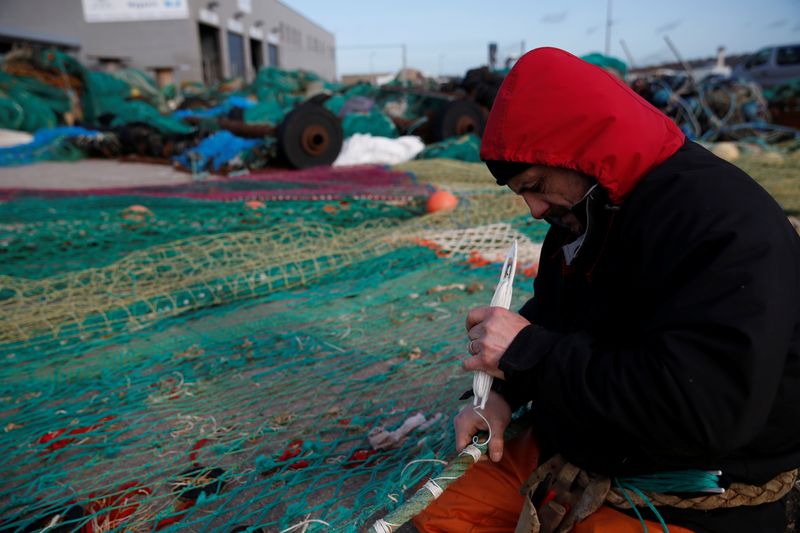 A fisherman repairs a fishing net on the dock of