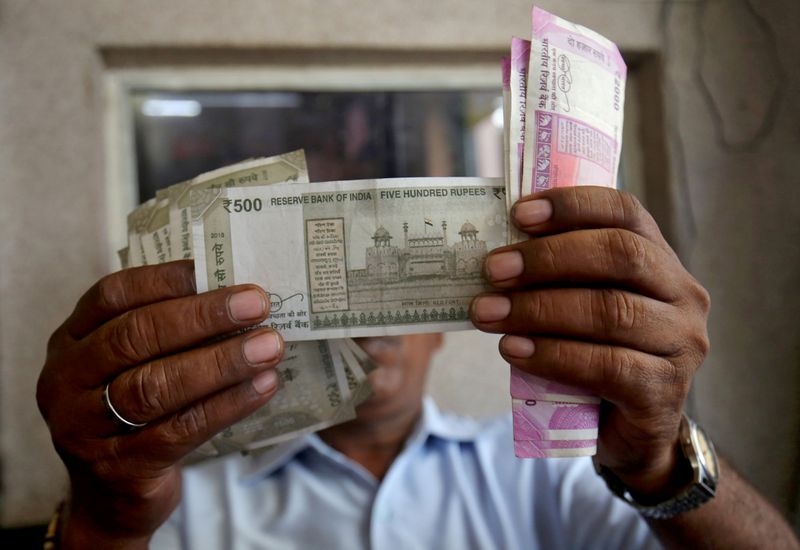 FILE PHOTO: A cashier checks Indian rupee notes inside a