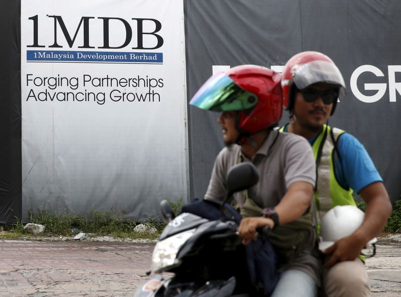 Motorcyclists pass a 1Malaysia Development Berhad (1MDB) billboard at the