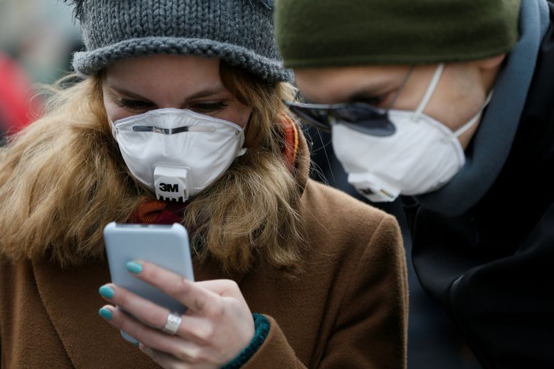 People wearing protective face masks use a smartphone on a