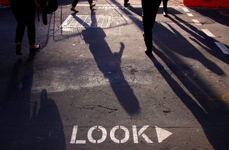 Shoppers and workers cast shadows as they cross an intersection