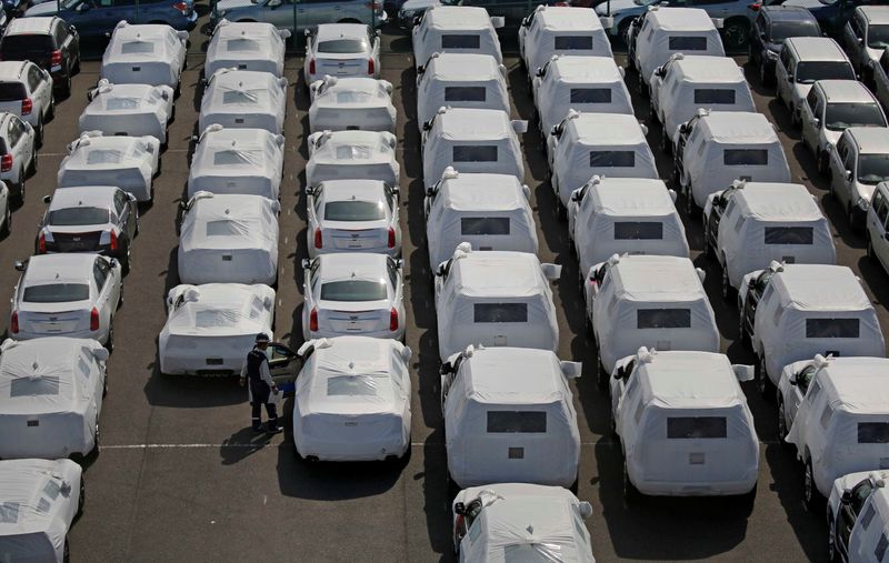 A man works among imported cars covered with a white