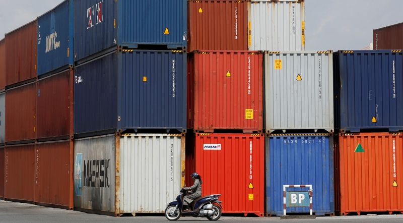 Woman rides a motorcycle as she passes containers at Hai