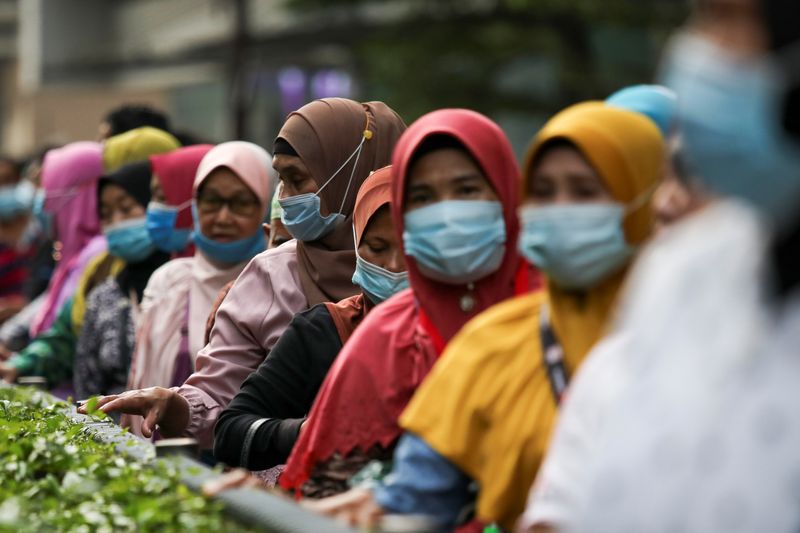 Passengers wearing protective masks wait in line at a bus
